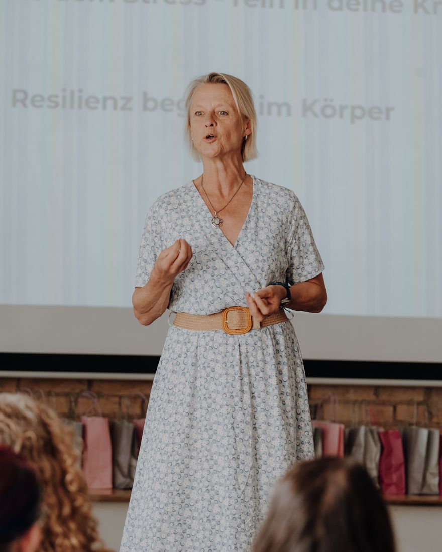 Tenna Dahl spricht vor Publikum, hinter ihr die Folie „Resilienz beginnt im Körper“