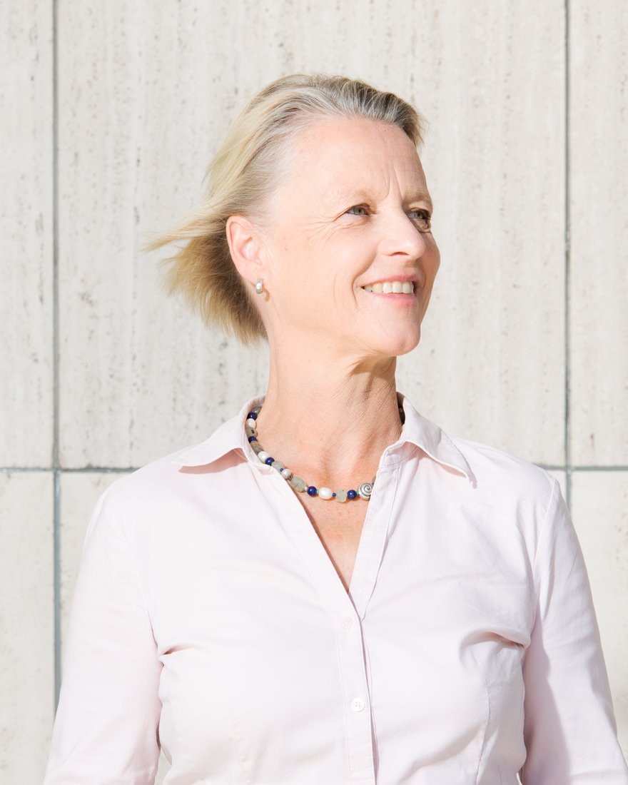 Dr. Tenna Dahl in front of a light stone wall, smiling and looking into the distance